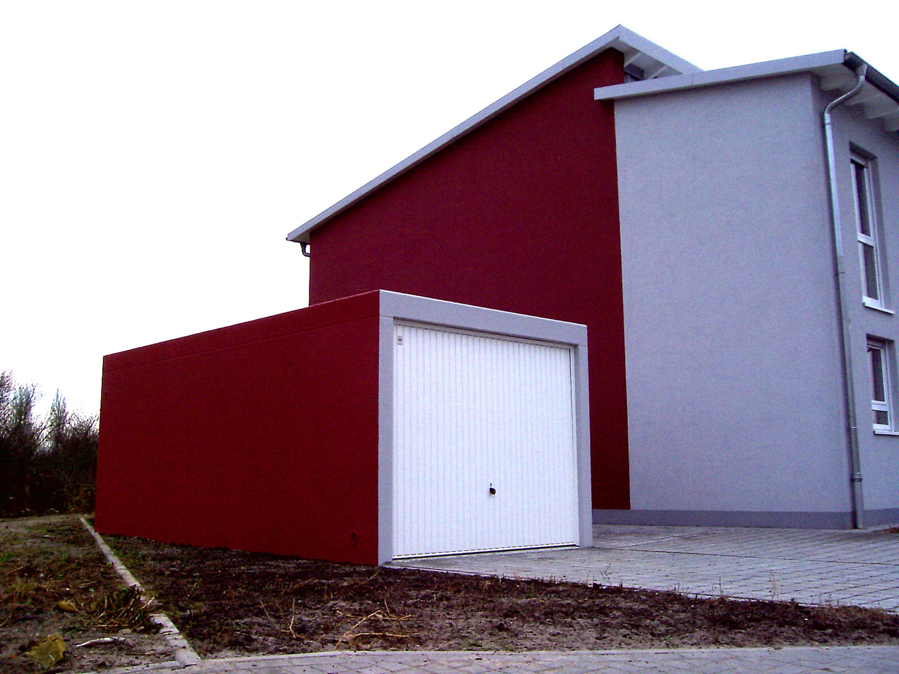 Eine Grötz Fertiggarage mit rotem Putz und weißem Schwingtor