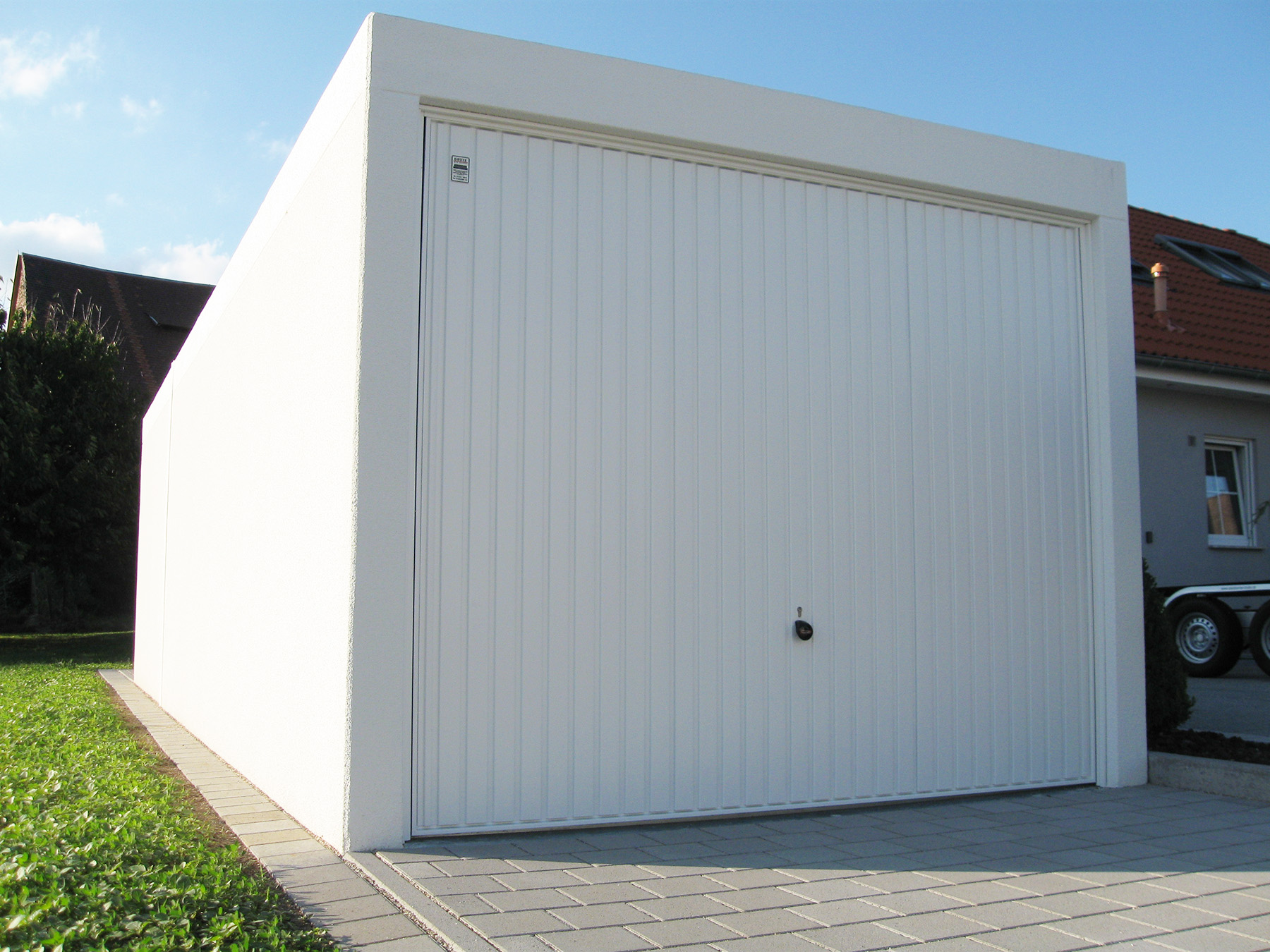 Eine Grötz Fertiggarage mit weißem Putz und weißem Schwingtor